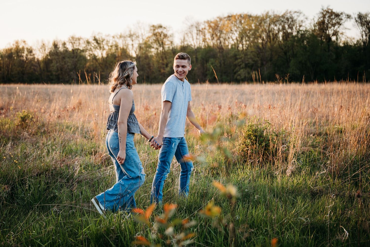 Two people in denim walking together through a golden sunlit field at sunset.