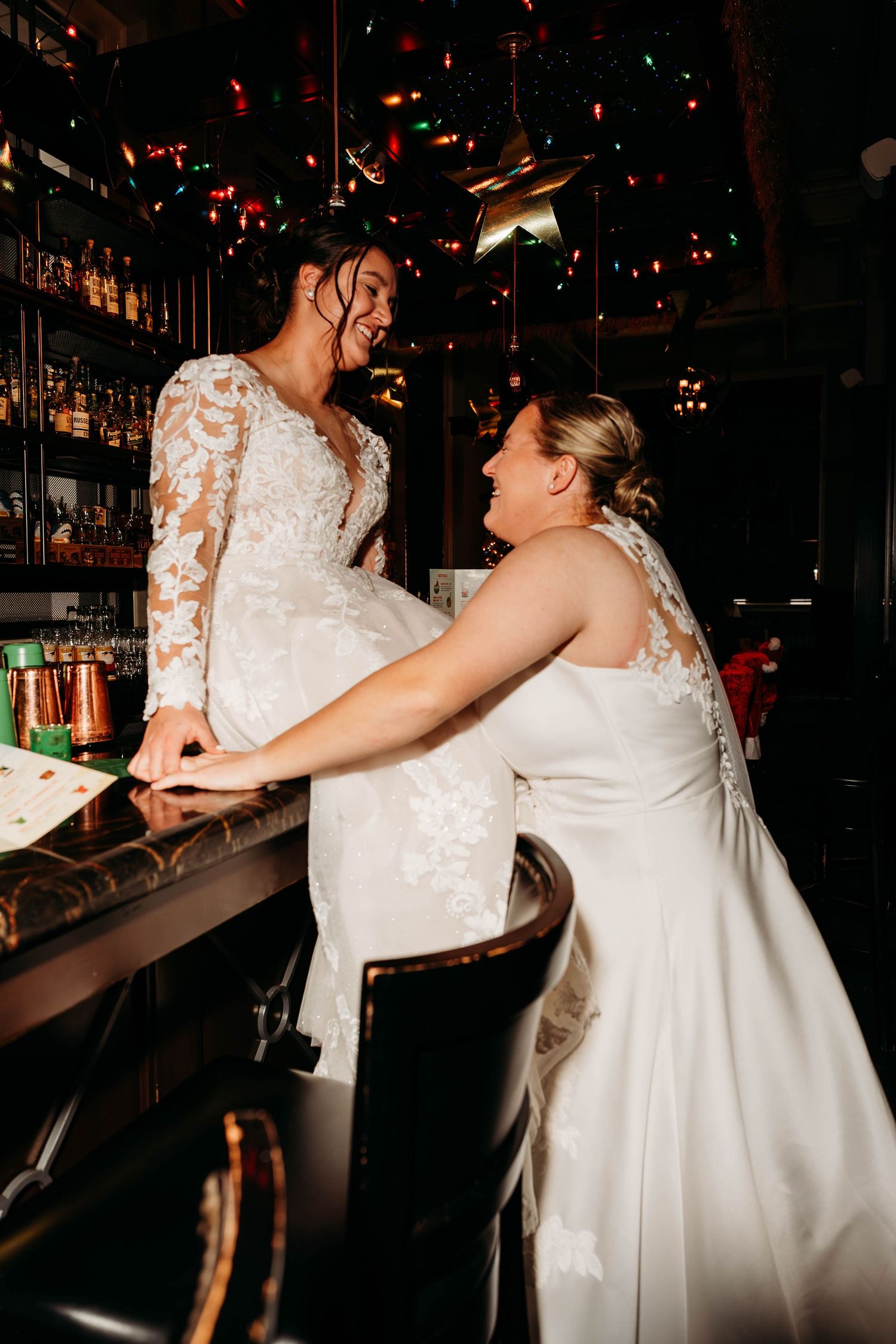 Couples dancing together in white wedding gowns under dim lighting at a reception.