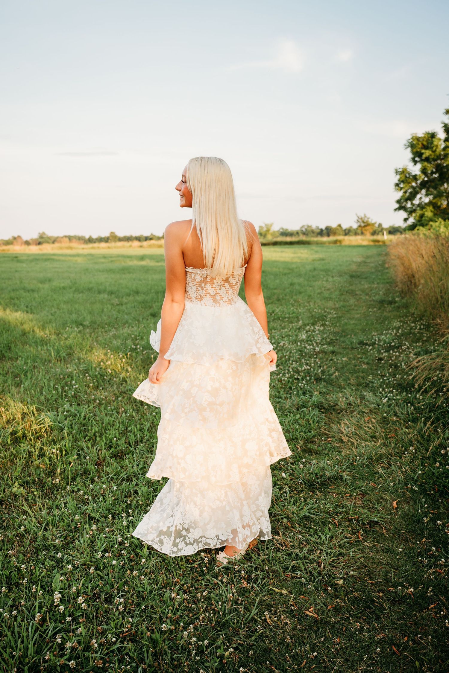Flowing white lace dress moves gracefully through a sunlit meadow filled with wildflowers.