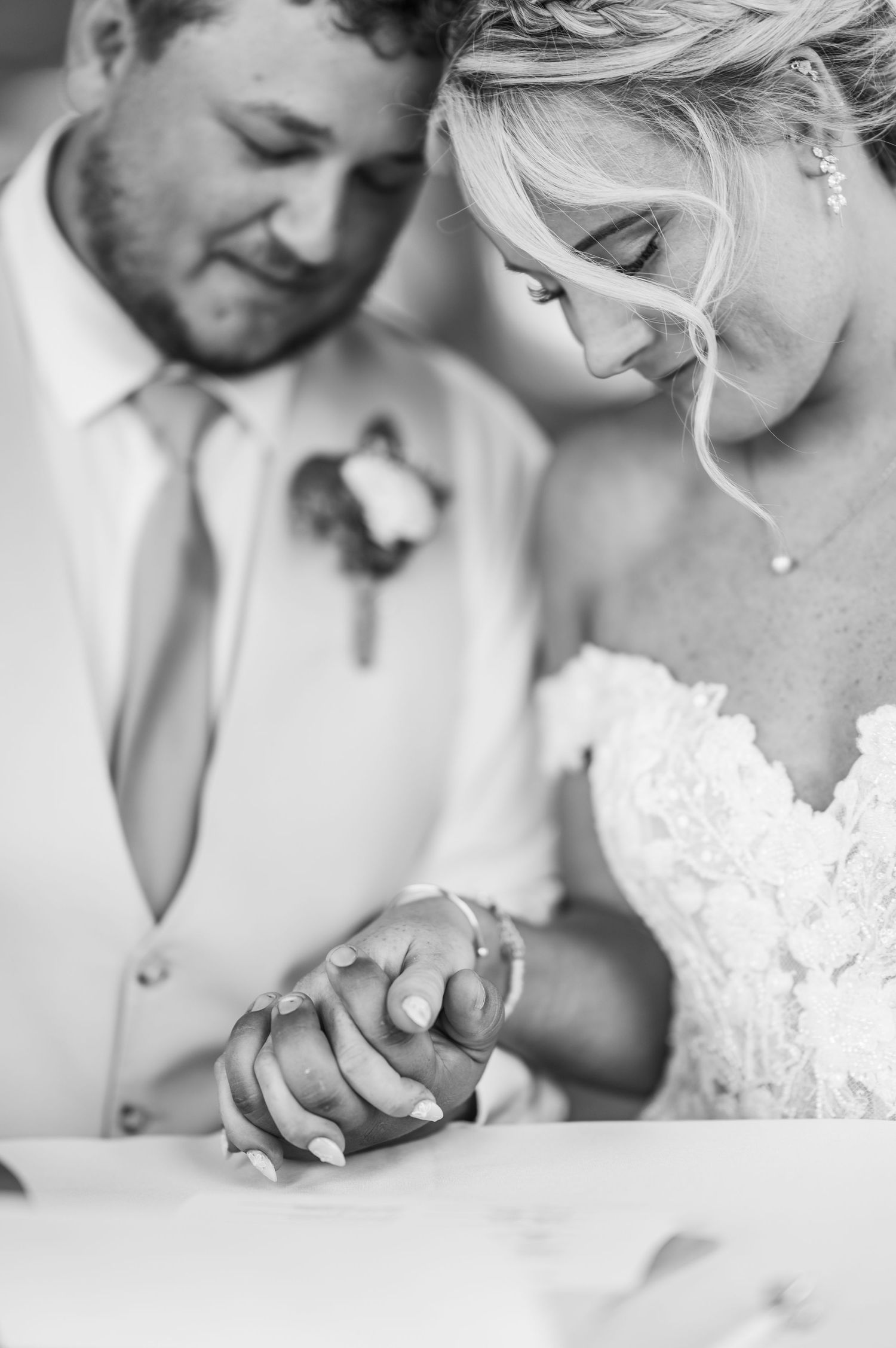 Black and white intimate wedding photo showing clasped hands and details of a lace bridal gown.