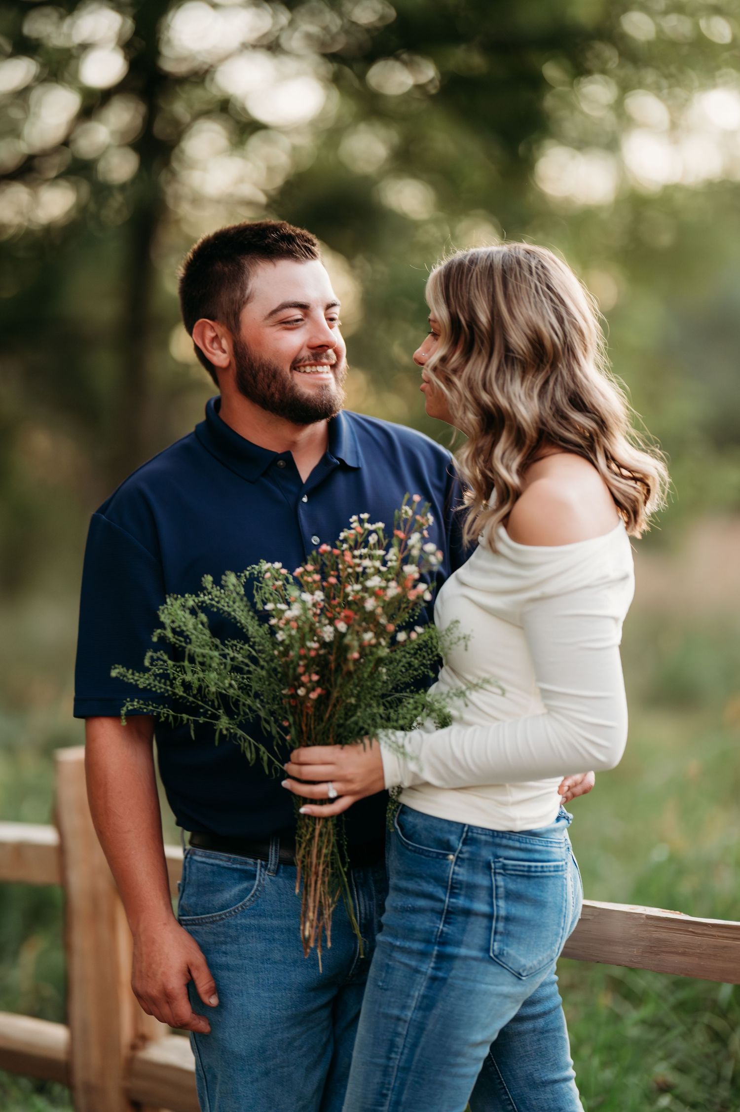 A couple shares tender moments outdoors while holding wildflowers during a romantic photoshoot in nature.