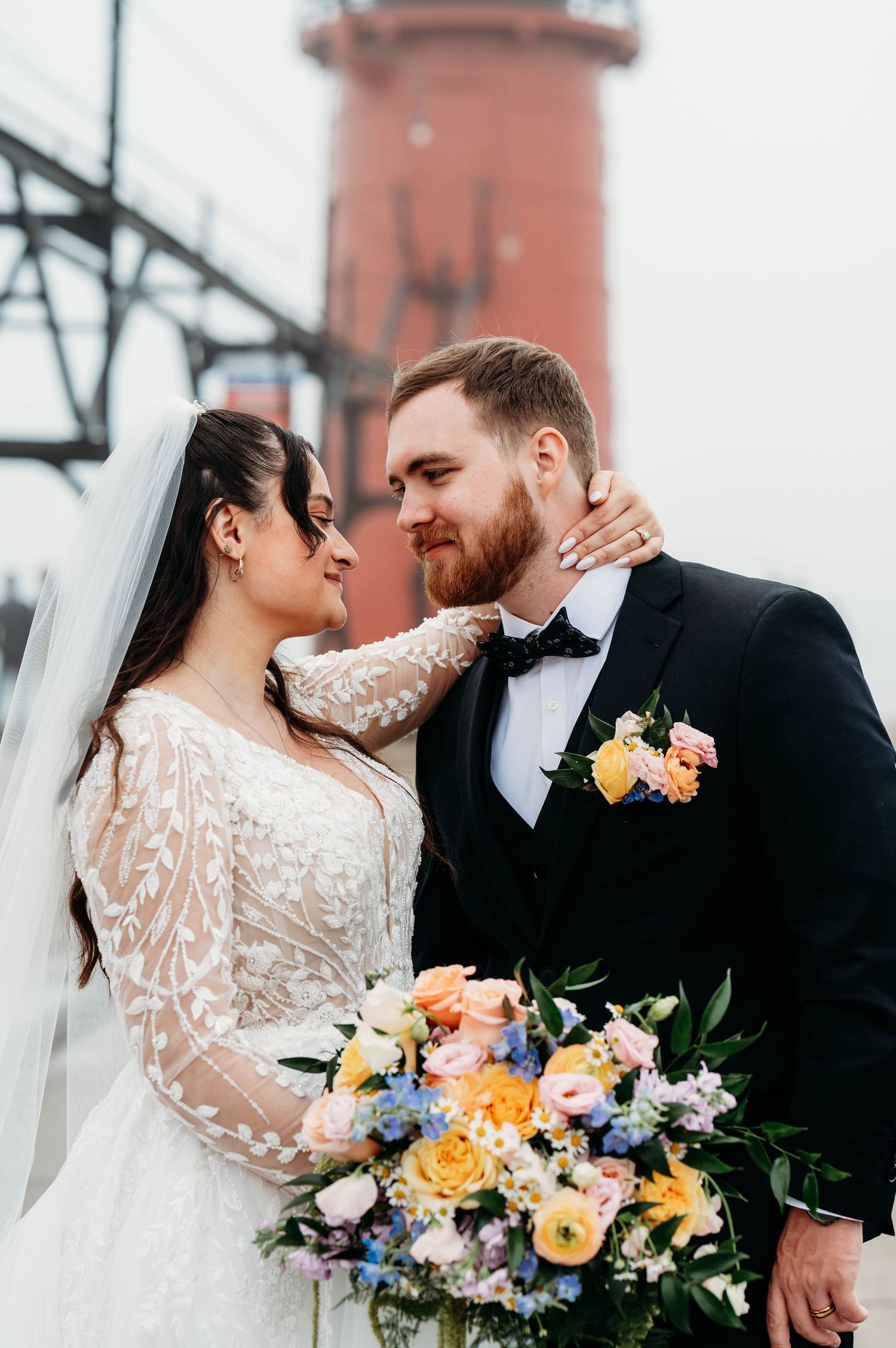 Bride and groom share romantic moment near lighthouse, bride holding colorful spring wedding bouquet.