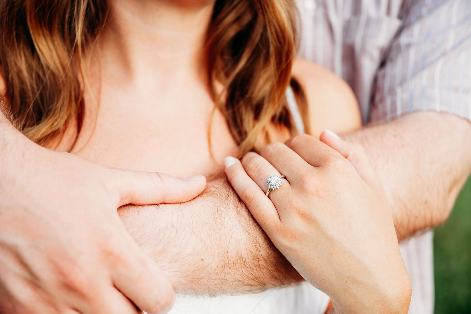 Close-up of a woman wearing a diamond engagement ring while embracing her partner outdoors.
