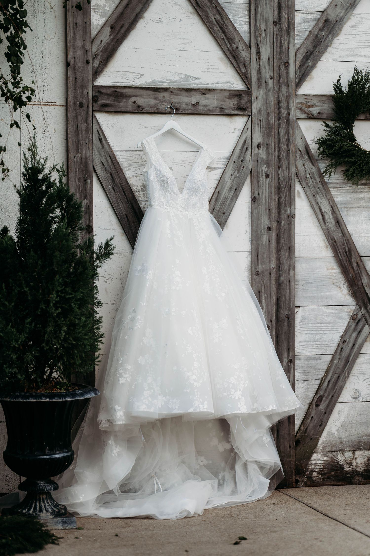 A white wedding dress with lace details hangs against a rustic wooden wall with cross beams.