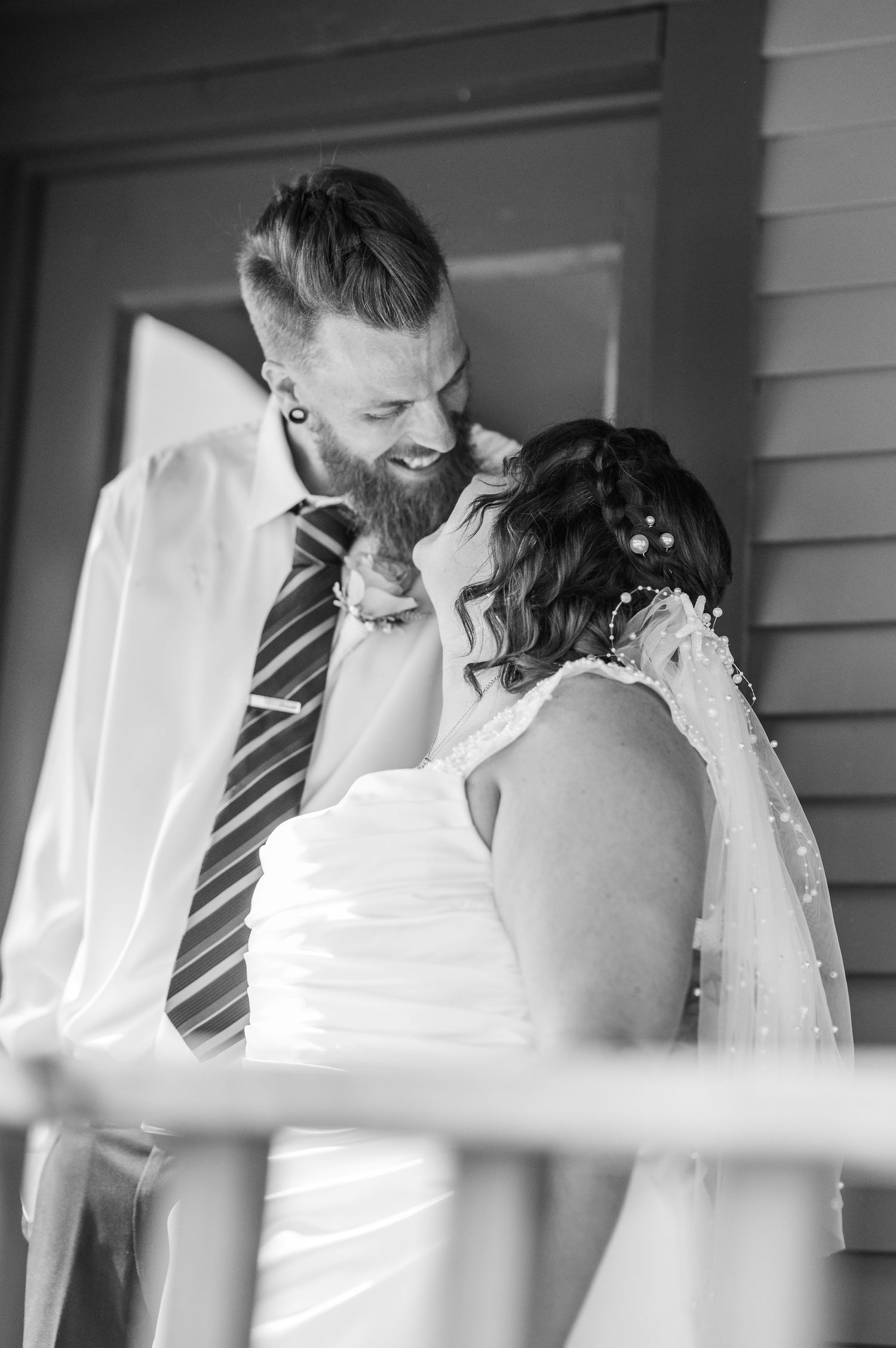 A tender black and white wedding moment captured through porch railings as a couple shares an intimate kiss.