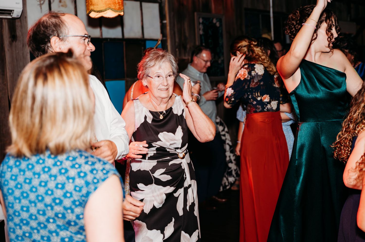 Guests dancing joyfully at a wedding reception, wearing elegant attire including floral dress and teal gown.