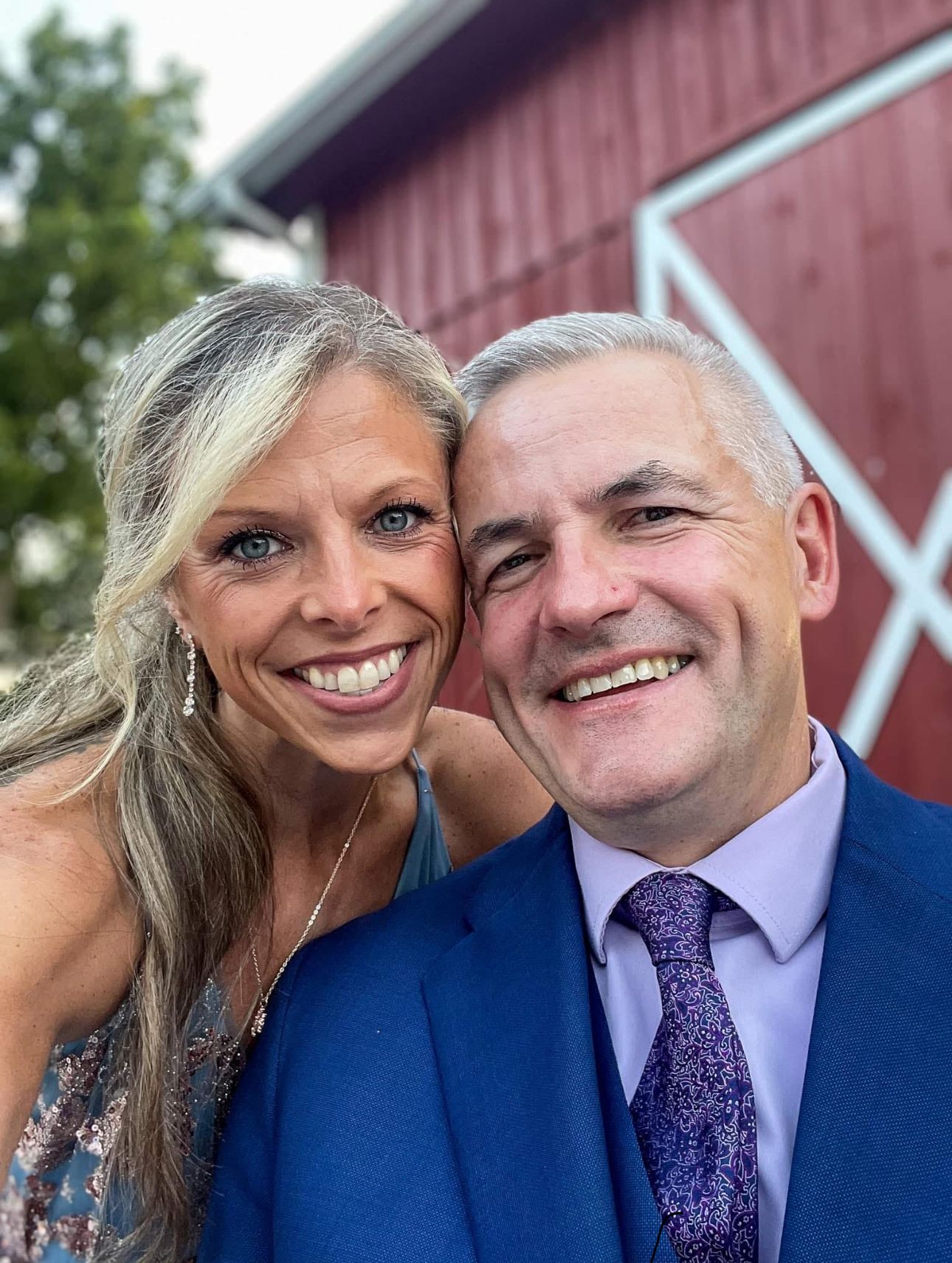 Happy couple smiling together in front of a red barn on a sunny day.