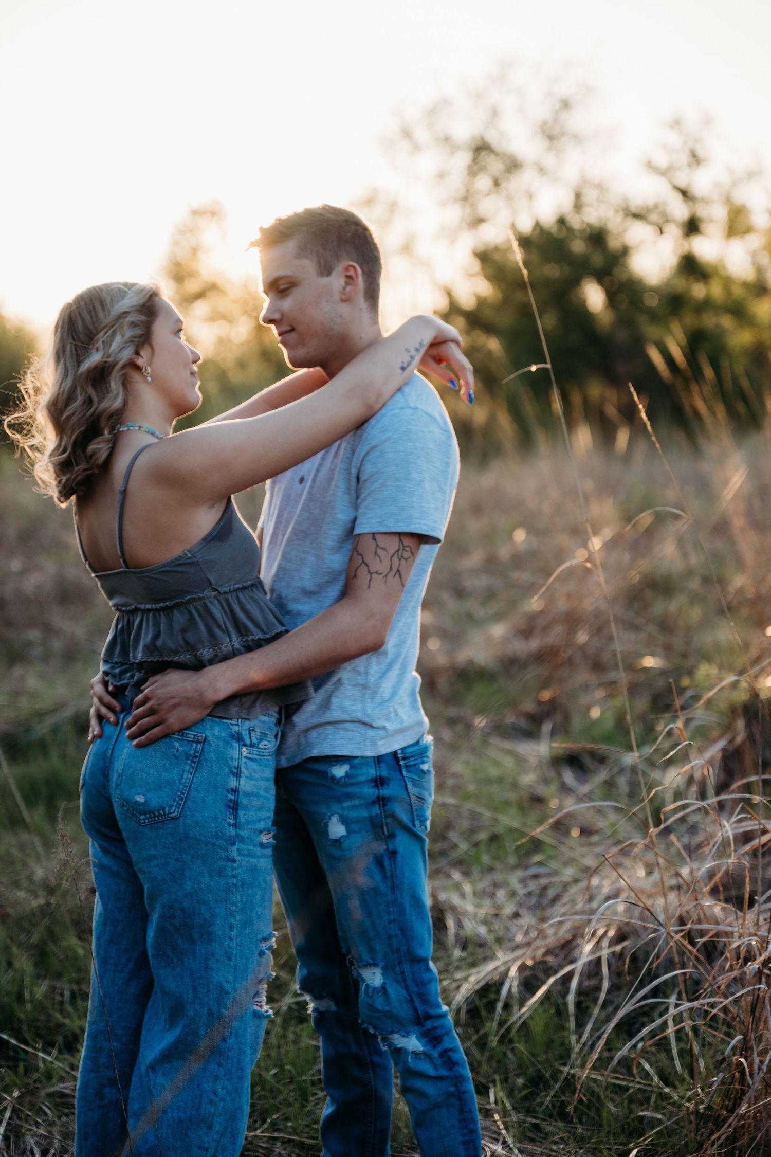 A couple embraces in a sunlit field during golden hour with tall grass swaying in the background.
