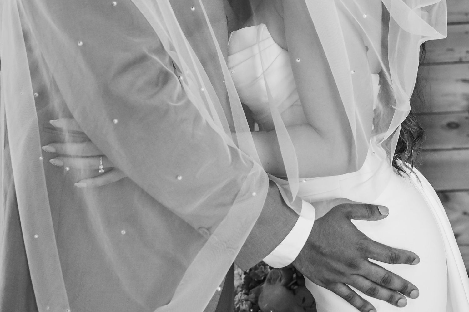 A bride and groom share a romantic kiss while standing in front of a white curtain backdrop at their wedding.