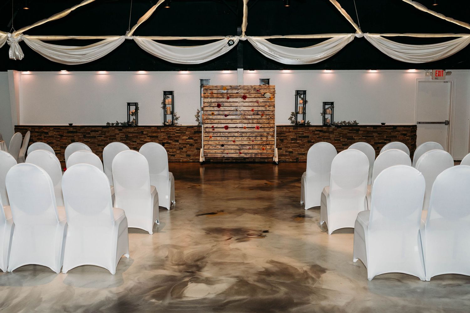 White chair covers line up in rows for a wedding ceremony in an industrial brick-walled venue.