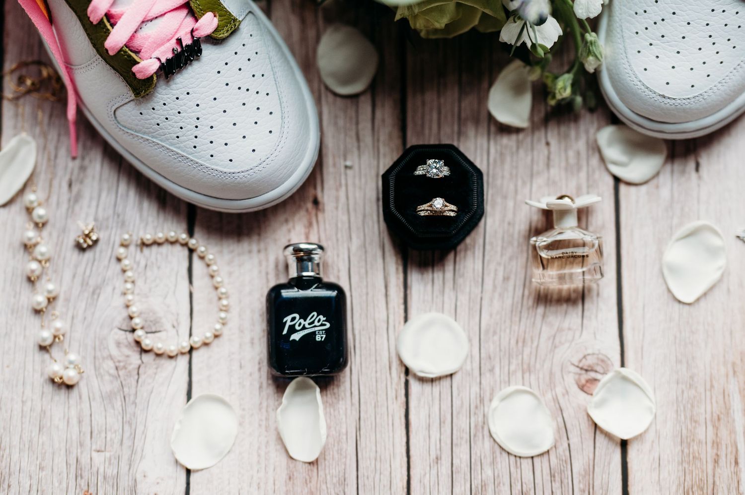 Flatlay of wedding accessories including white shoes, perfume bottles, and floral decorations on rustic wooden background.
