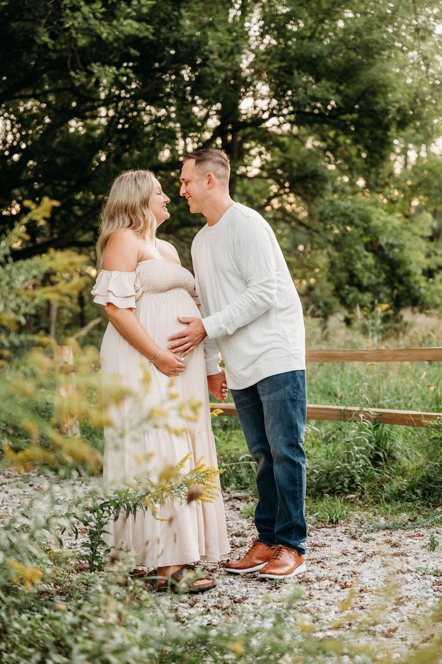 Couple in white outfits embracing during outdoor maternity photoshoot among scattered flower petals.