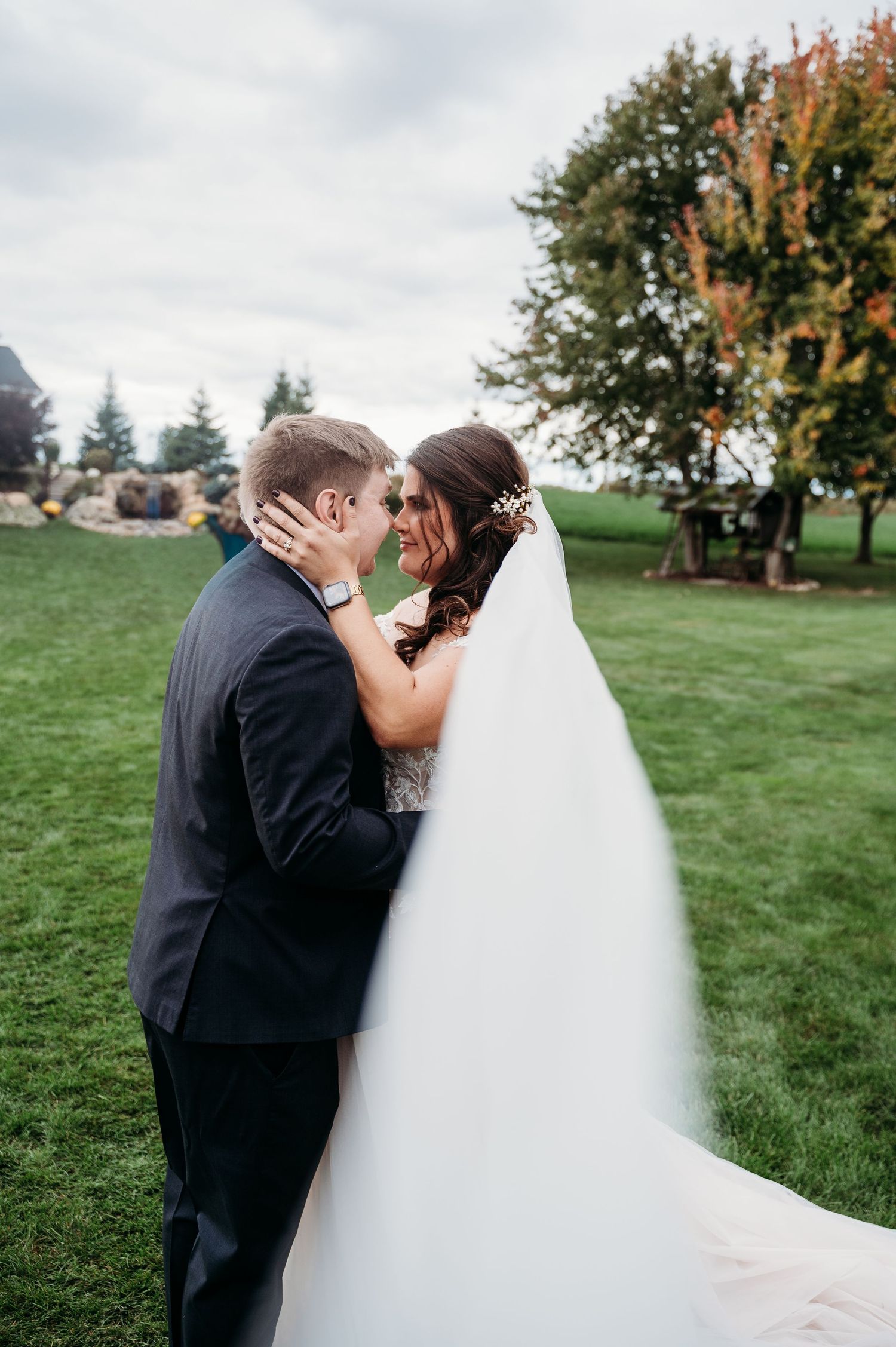 Newlyweds share a romantic kiss on a grassy hillside during their outdoor autumn wedding celebration.