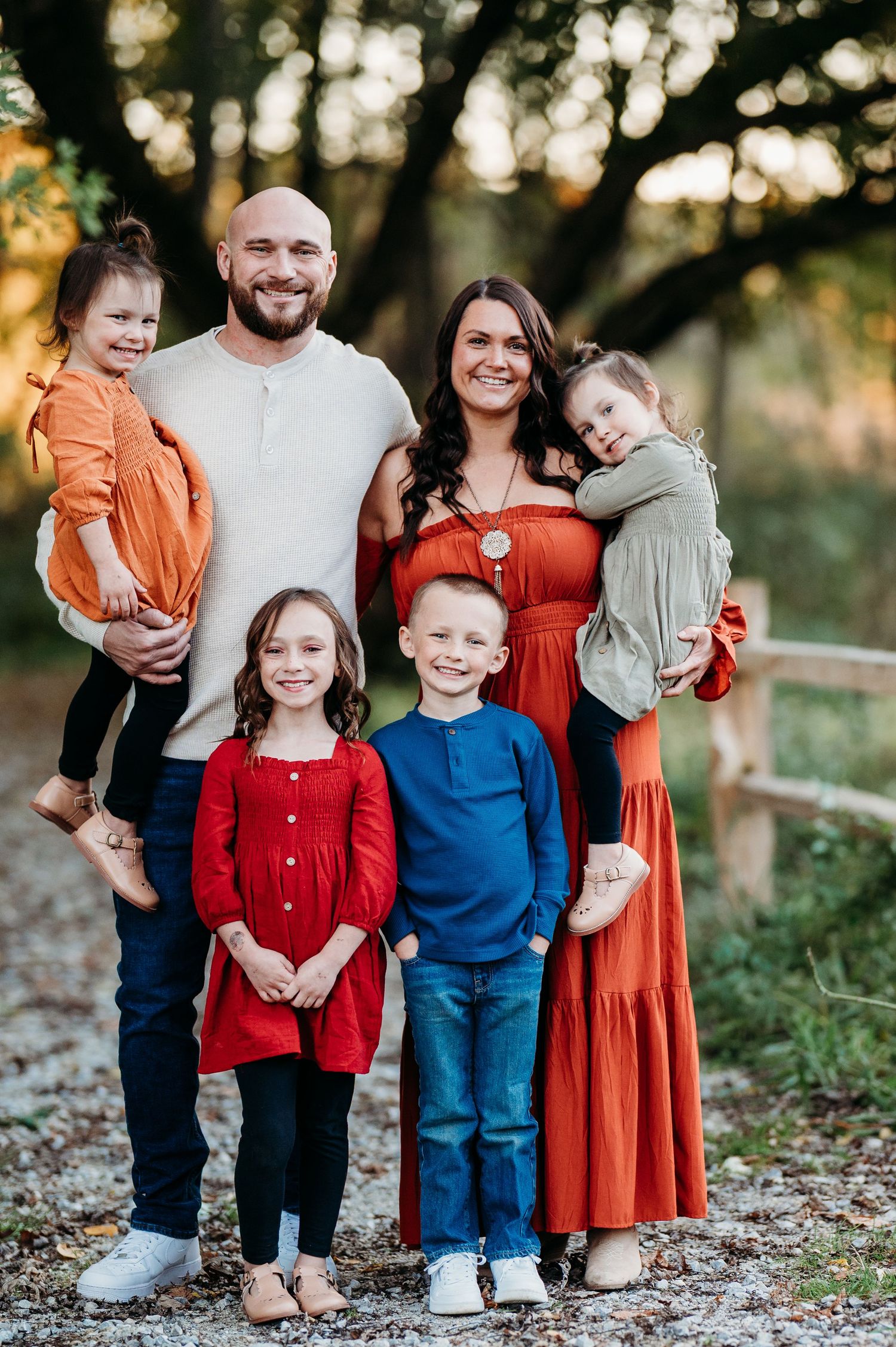 Happy family of six posing outdoors in coordinated fall outfits, parents holding toddlers while two children stand in front.