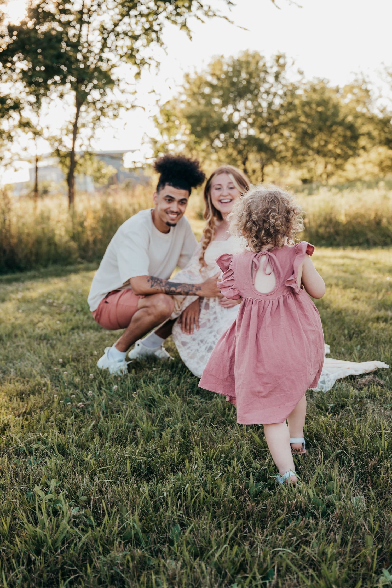 Family lounges on grass during golden hour outdoor photoshoot in summer park setting.