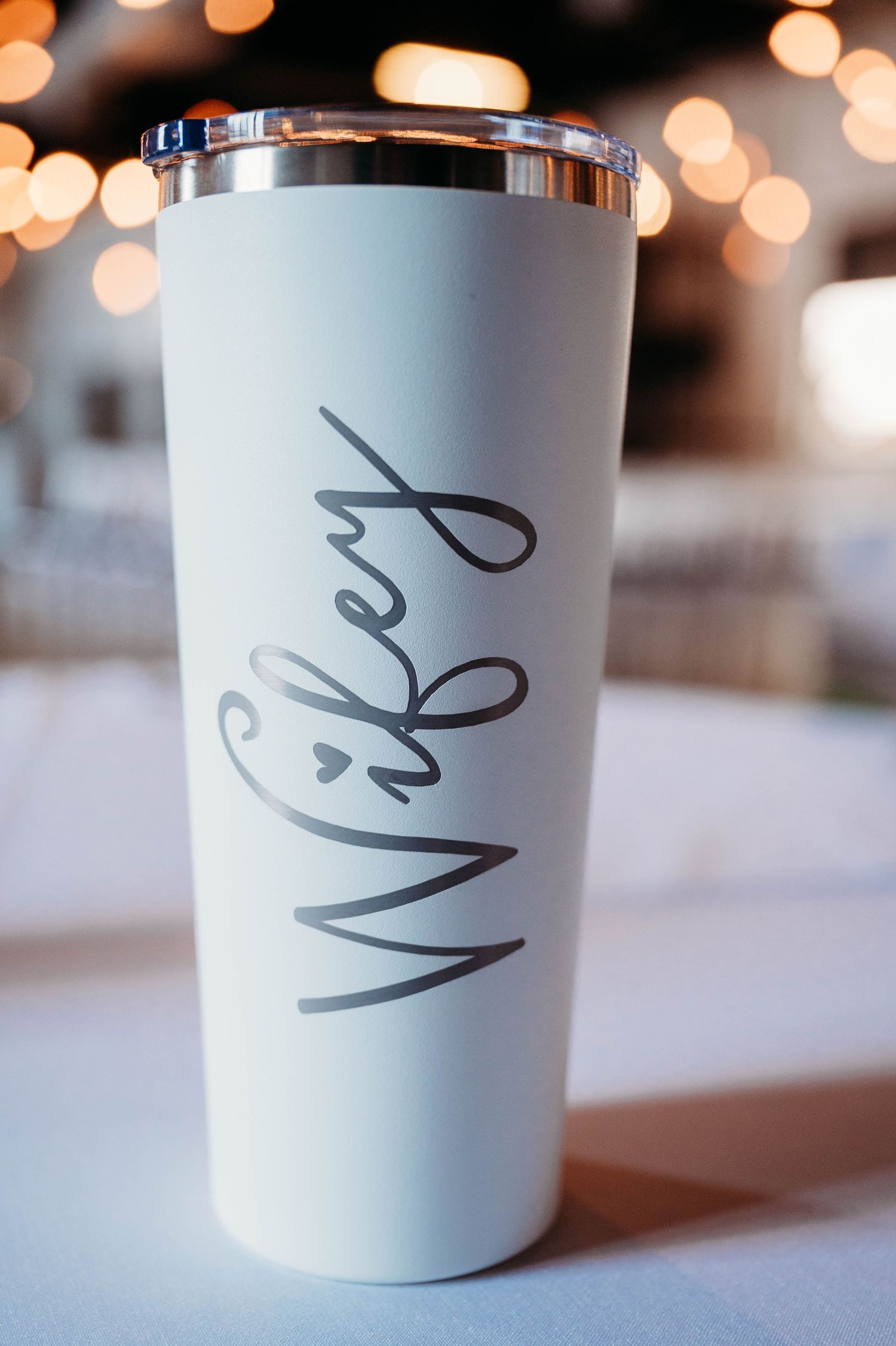 White travel tumbler with 'Wifey' script text against a bokeh background.