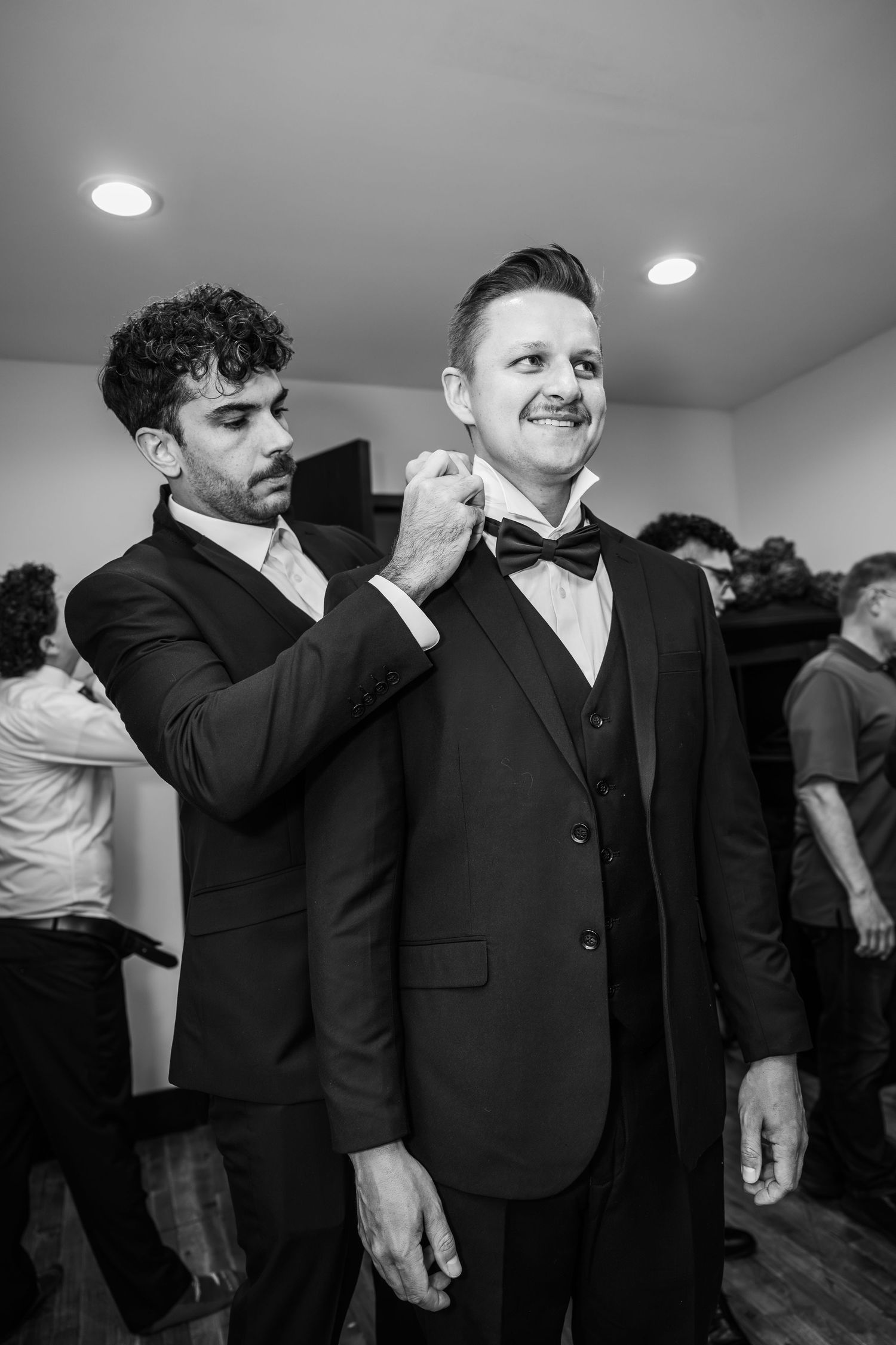 Groomsmen in black suits share emotional moments before a wedding ceremony.