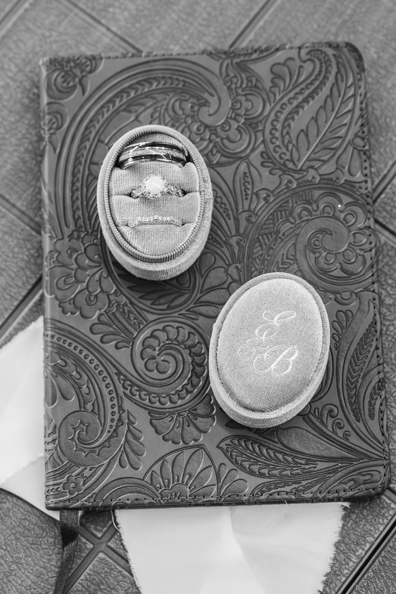 Black and white photo of diamond engagement ring in oval velvet box with monogrammed EB initials on embossed journal.