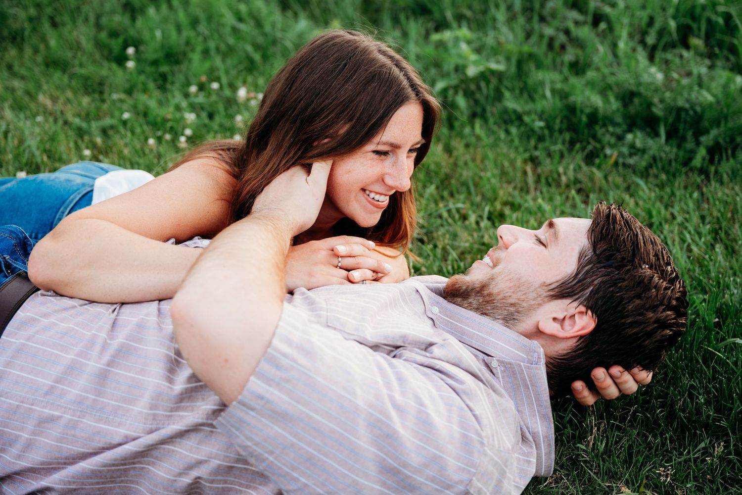 Happy couple lying on green grass, woman smiling at man lying on his back, sharing a joyful romantic outdoor moment.