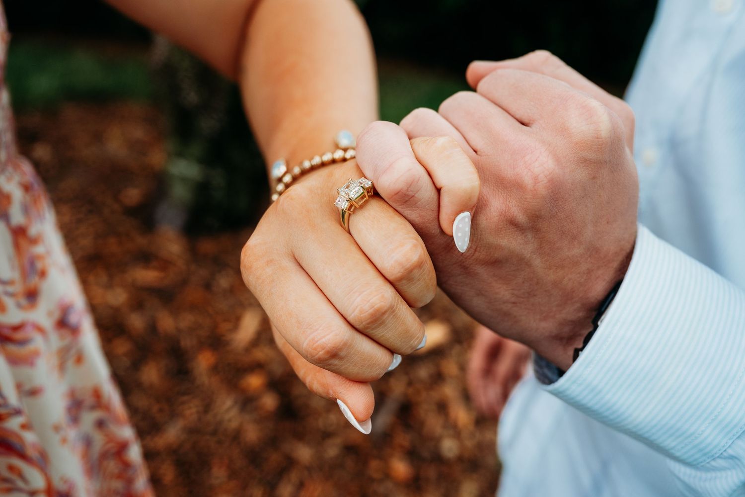Close-up of couple holding hands with a gold diamond engagement ring and pearl bracelet on the bride's hand.