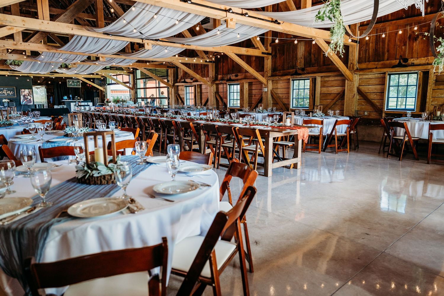 Rustic wooden barn venue decorated for a wedding reception with elegant table settings and exposed beam ceiling.