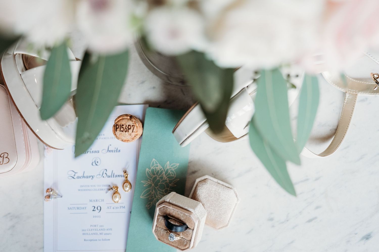 Wedding invitation details with soft mint green leaf decorations and floral elements laid on a white surface.