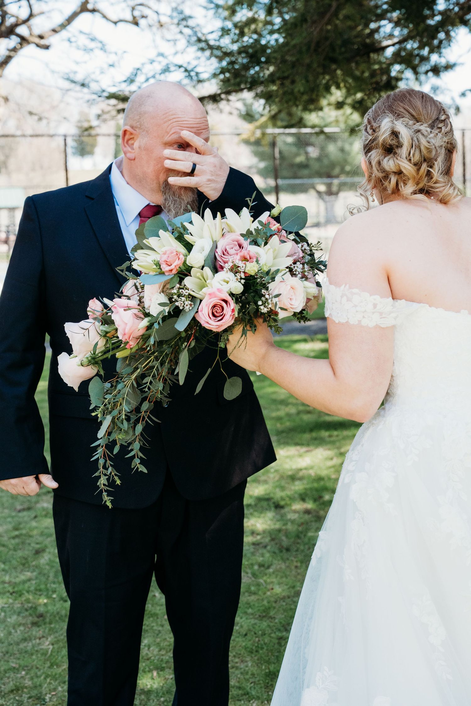 A beautiful wedding first look moment with a white bridal gown and bouquet of pink roses and greenery.