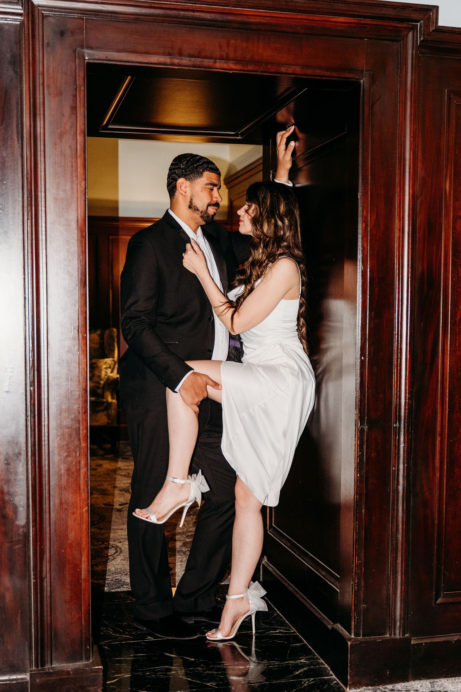 Romantic wedding couple shares intimate moments in a dimly lit hallway with rich wooden paneling.