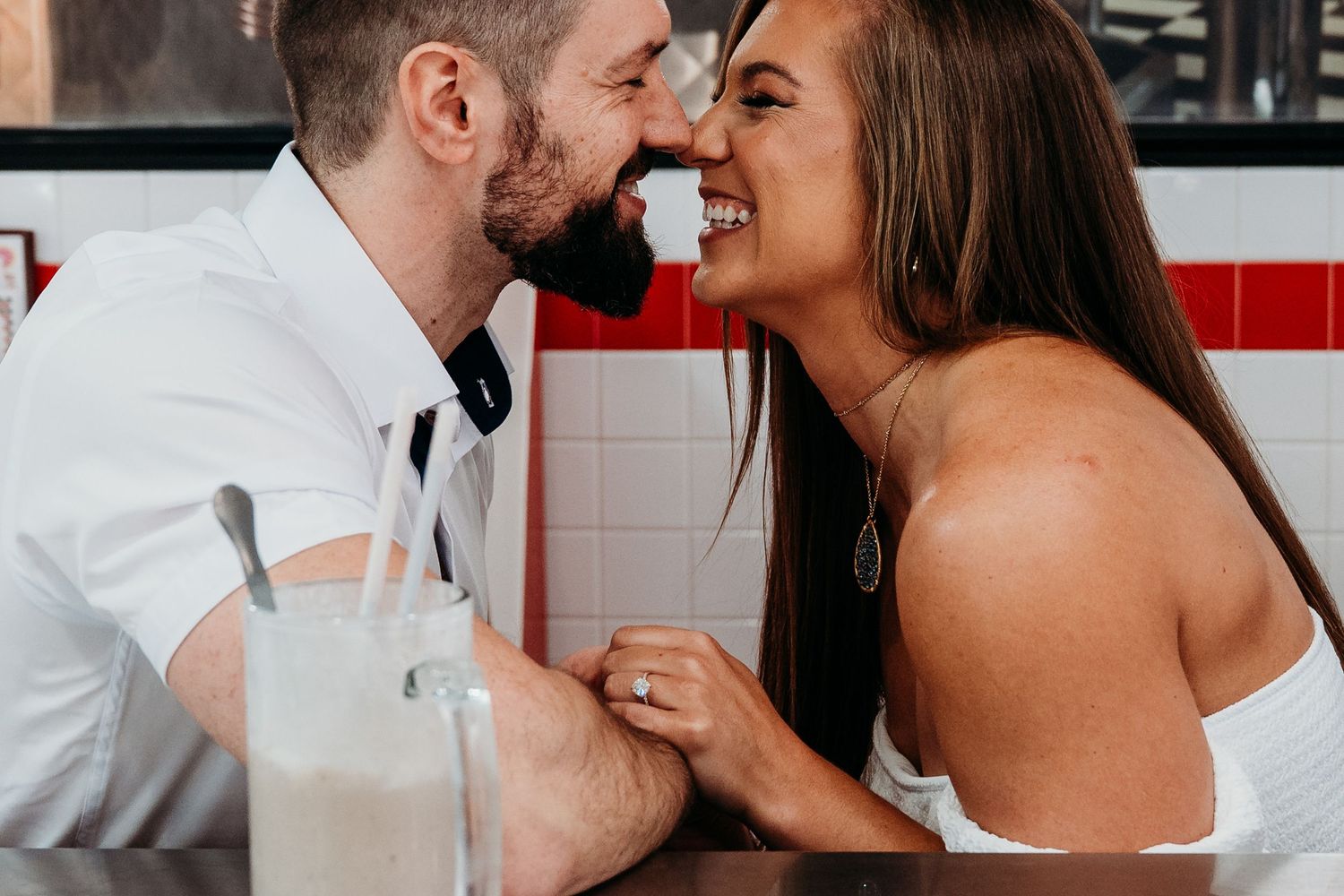 Laughing couple sharing intimate moment while drinking milkshakes.