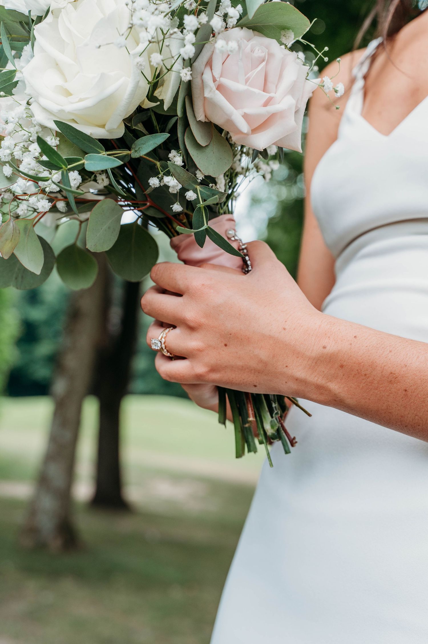 A bridal bouquet of white and blush roses with eucalyptus greenery held against a white wedding dress.