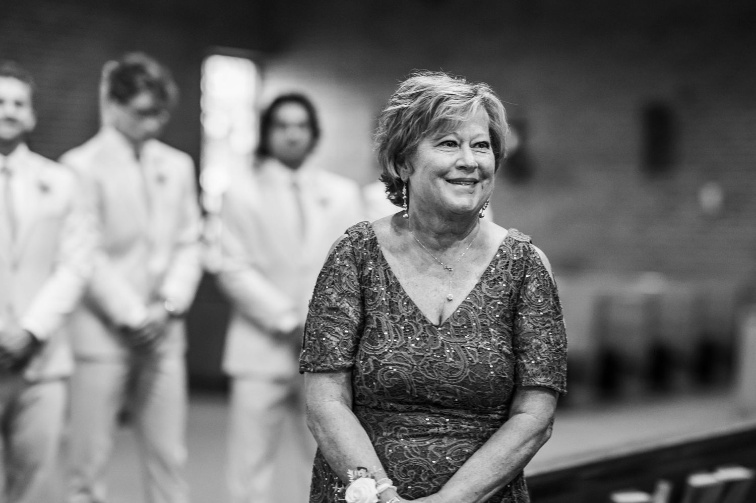 A black and white candid photo shows someone in a patterned dress smiling warmly at an indoor event.
