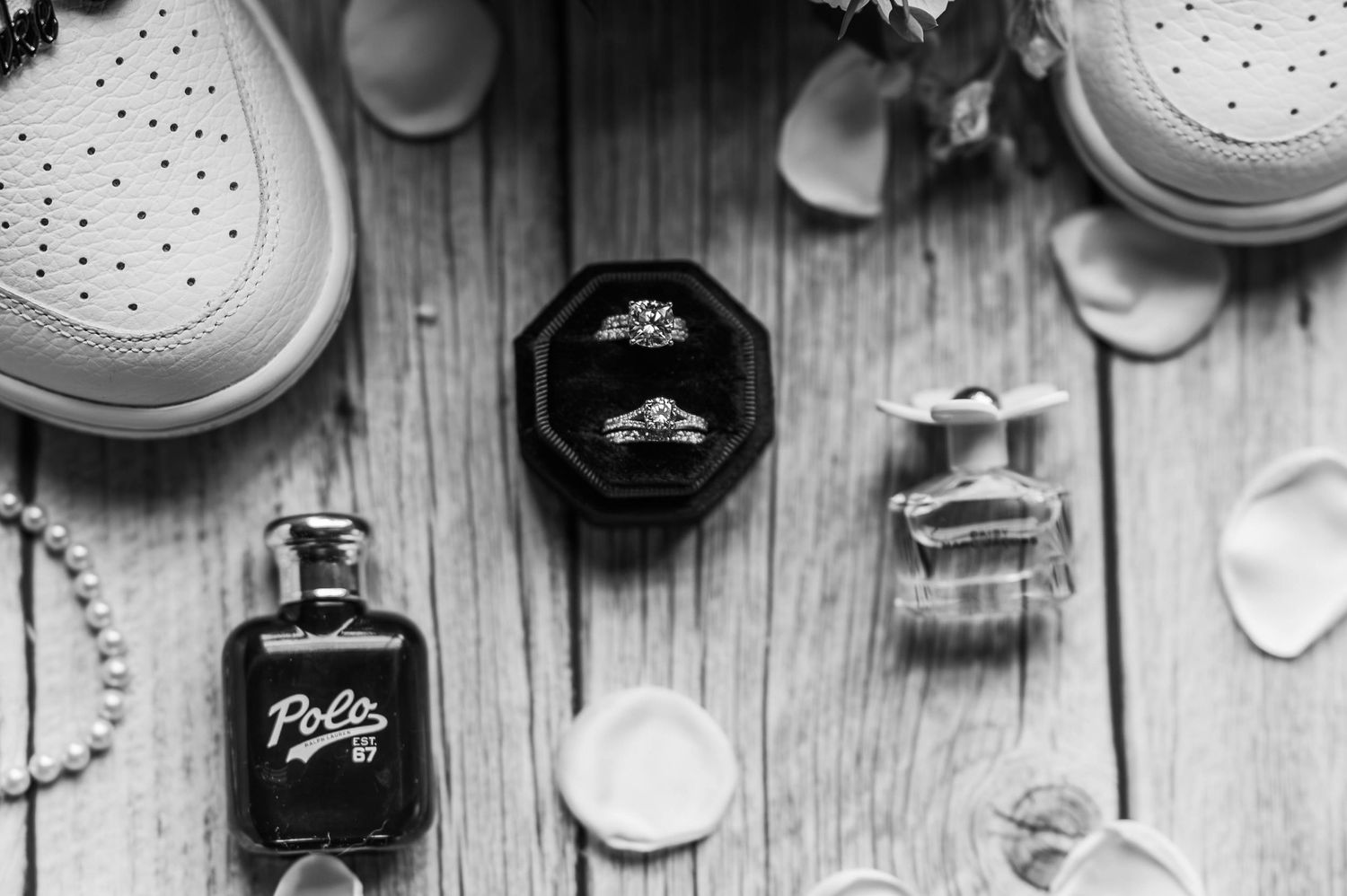 Wedding details flatlay with white sneakers, perfume bottles and rings on wooden background.