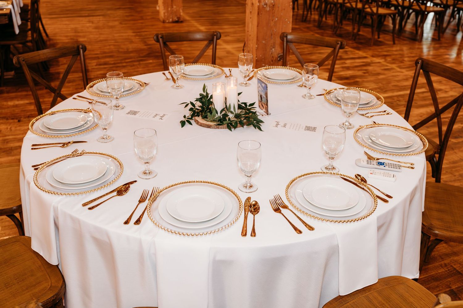 Wedding reception setup with round tables dressed in white linens and formal place settings in rustic wooden venue.