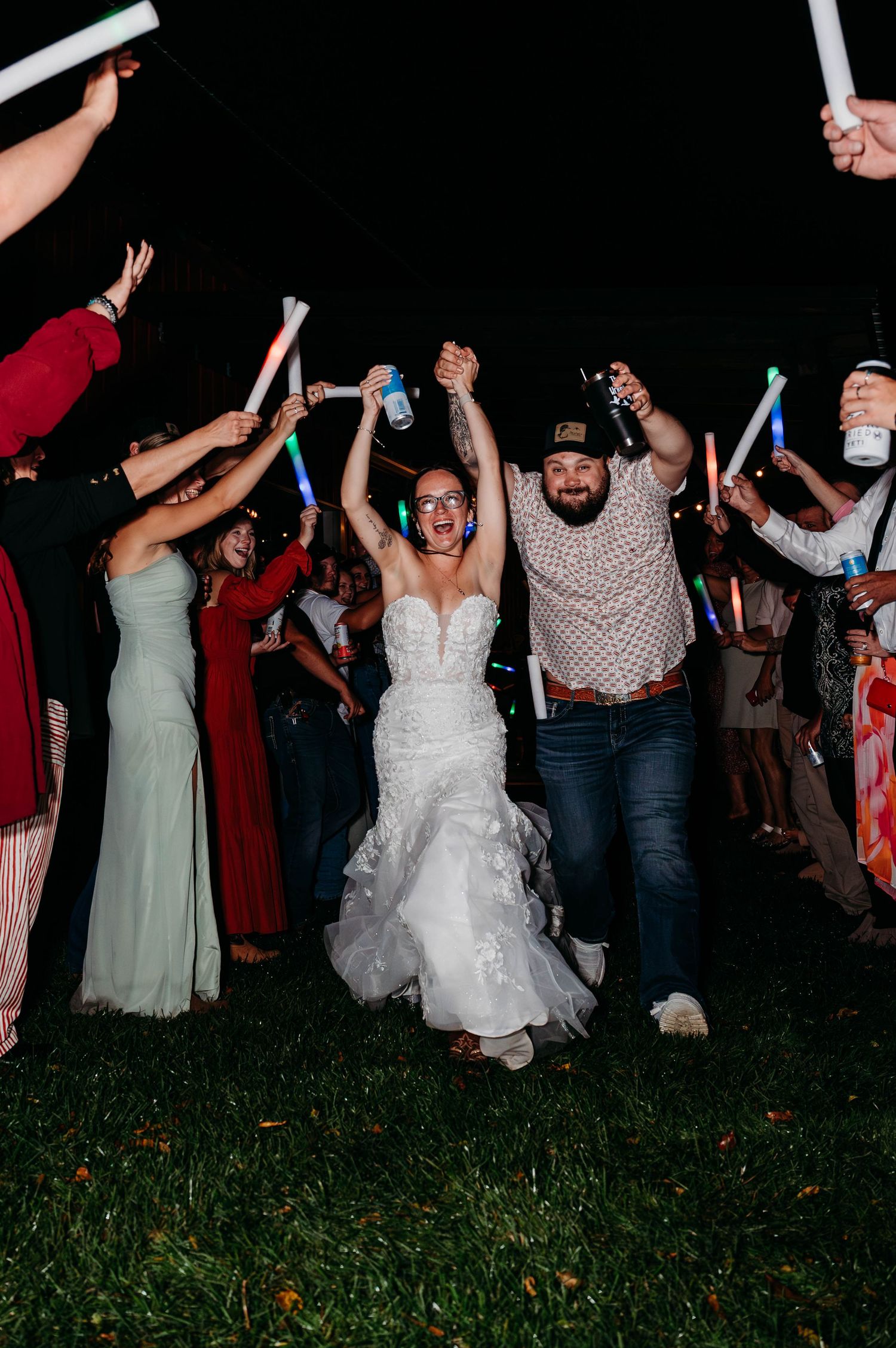 Wedding celebration at night with guests dancing and waving light sticks on a grassy field.