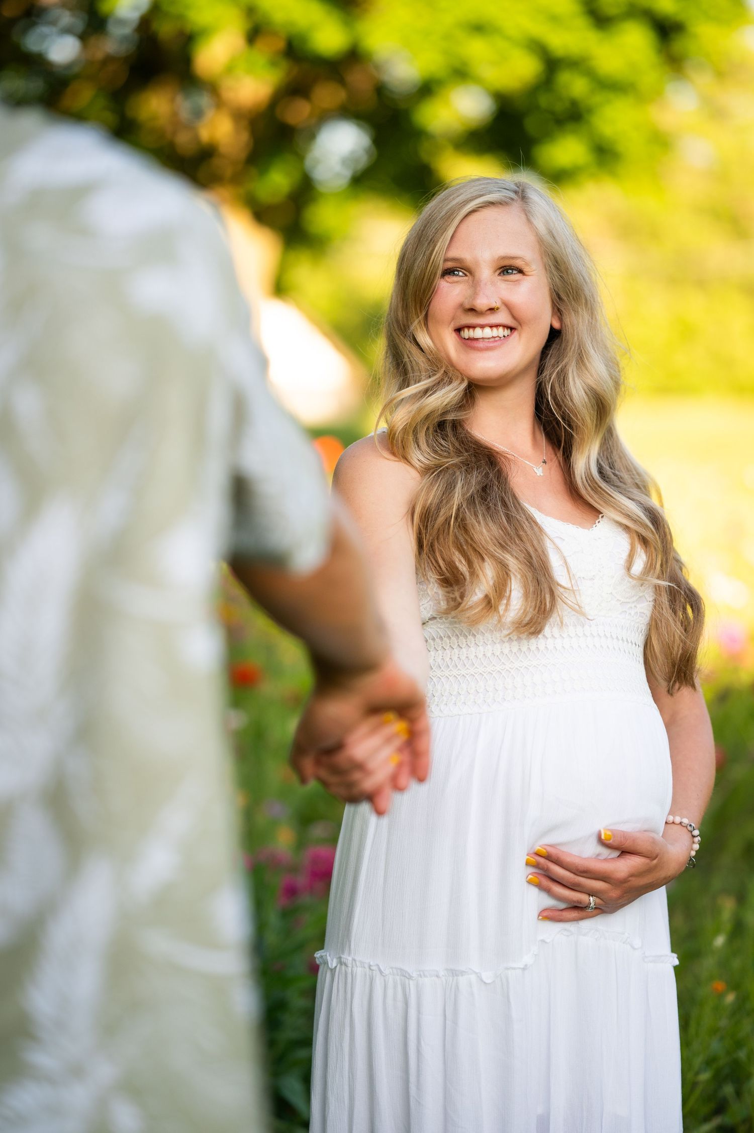 Maternity photo of woman in white dress standing in garden setting.