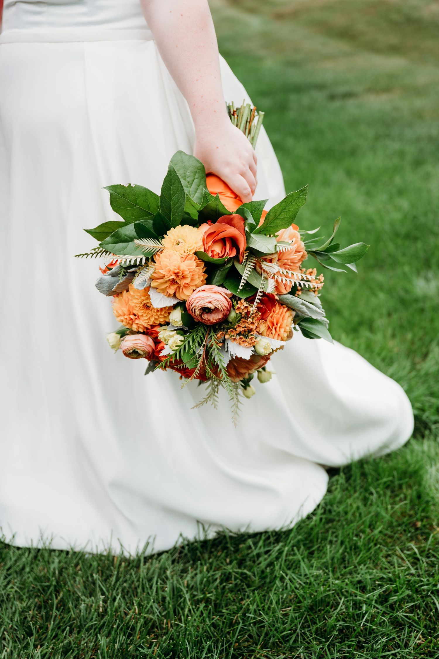 Close-up of a peach and coral bridal bouquet with greenery against lush grass.