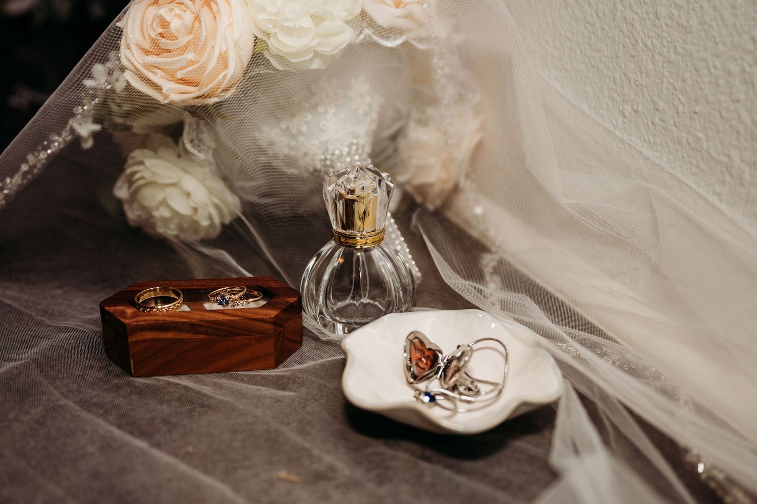 Elegant wedding rings displayed with soft pink roses and delicate lace details on a textured surface.