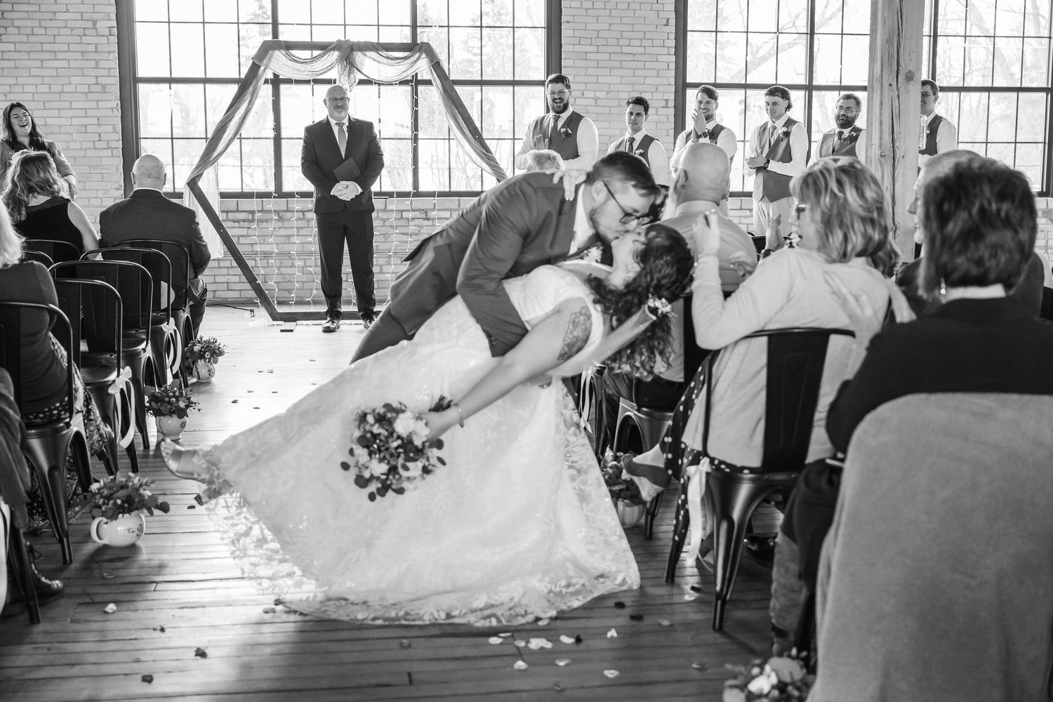 A wedding ceremony in a bright industrial venue with large windows and guests seated in rows.