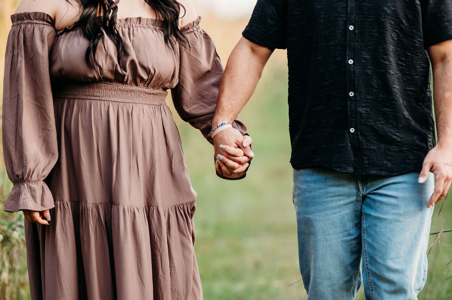 Couple holding hands outdoors, woman in brown tiered maxi dress, man in black shirt and jeans.