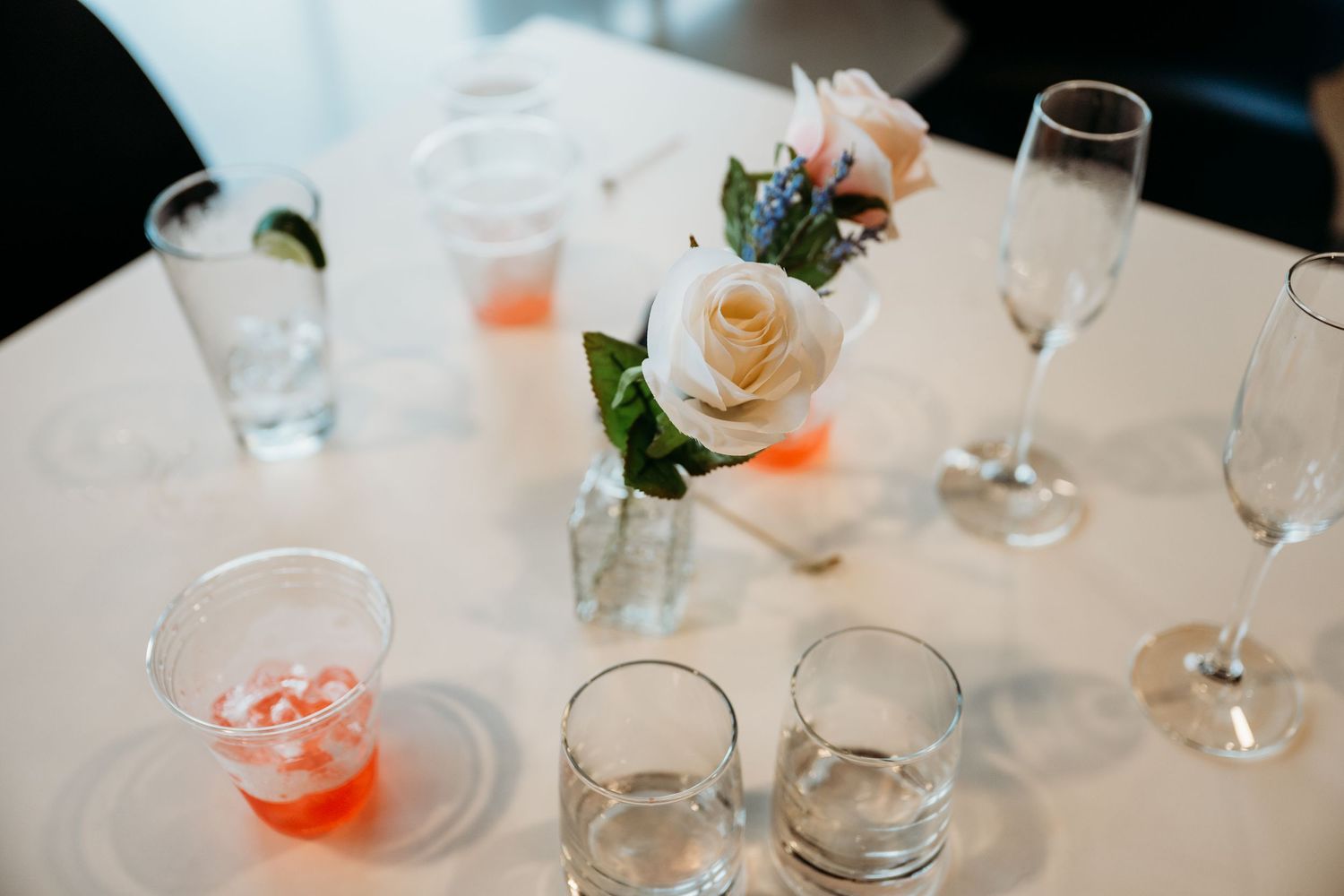 A wedding reception table setting with white roses, glassware, and soft lighting creating an elegant atmosphere.