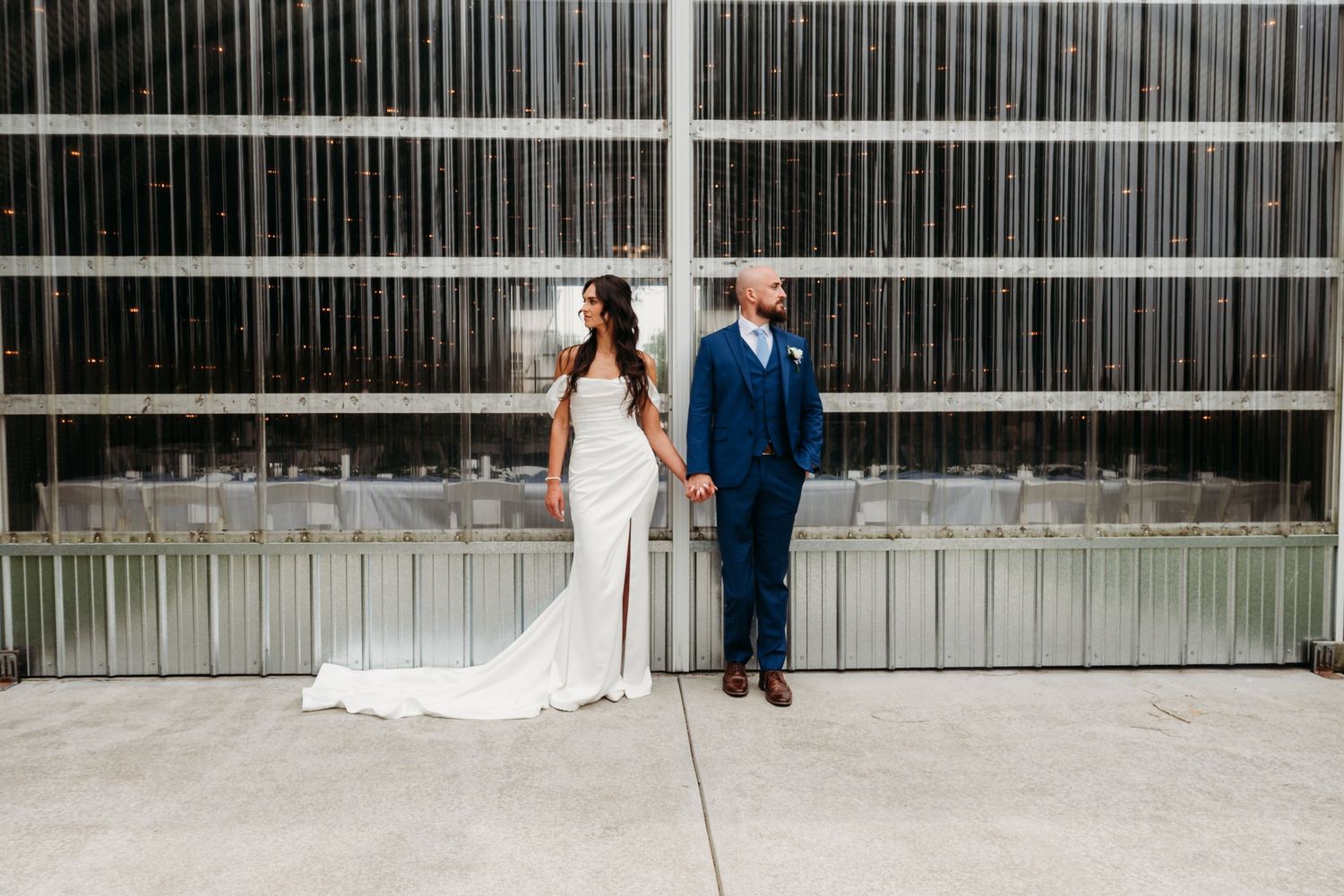 A couple stands together in various poses against an industrial metal wall background for their outdoor wedding photos.