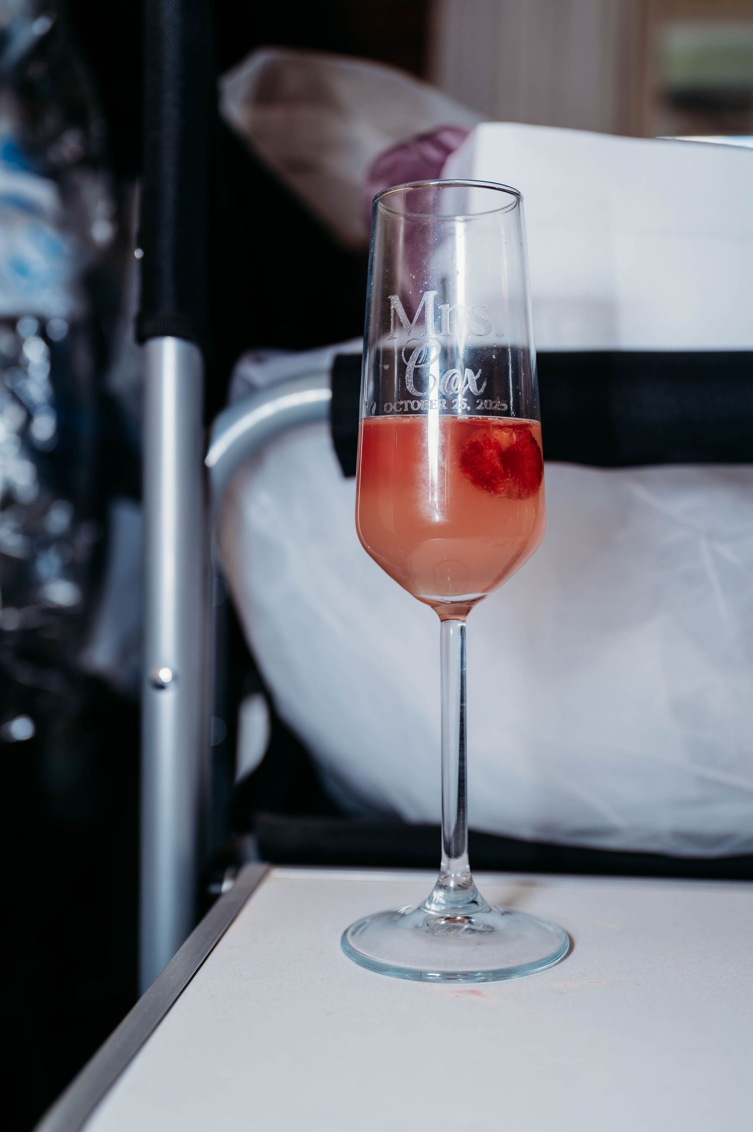 A glass of pink champagne or cocktail sits elegantly on a white surface in soft lighting.