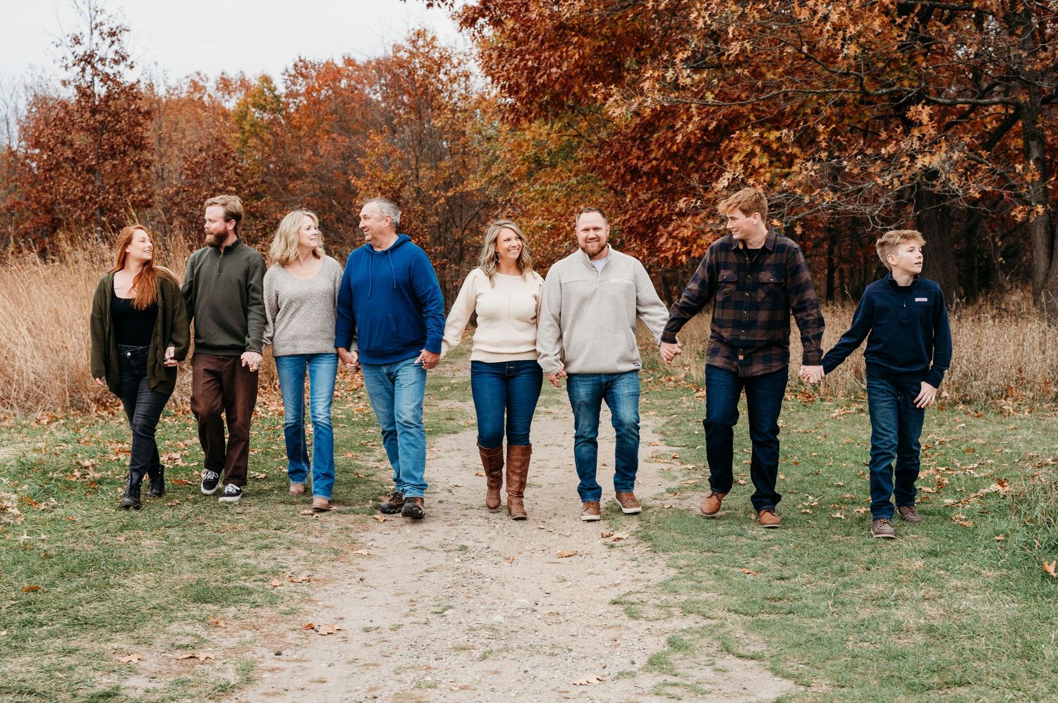 A group of people walk together along a dirt path surrounded by autumn trees with orange foliage.