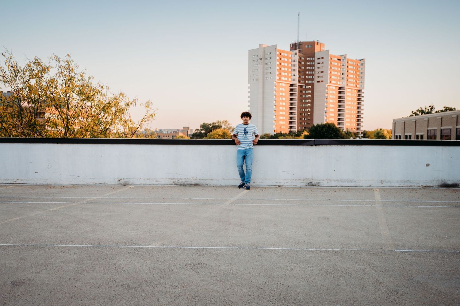 A person in blue clothing stands on a rooftop against a backdrop of a tall apartment building at sunset.