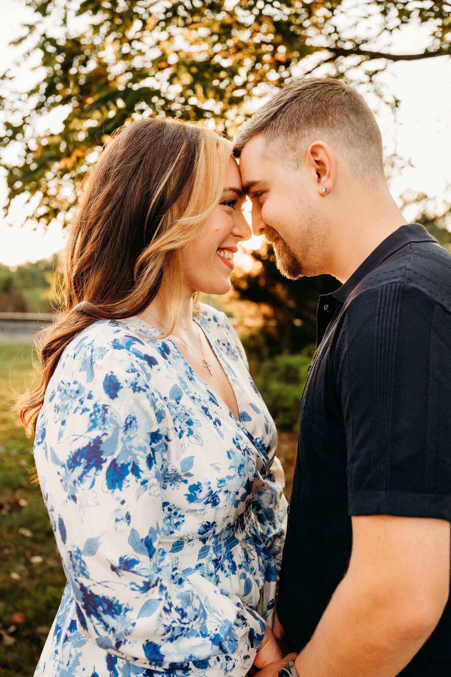 A romantic couple embraces during a golden hour photoshoot in a park with autumn trees in the background.