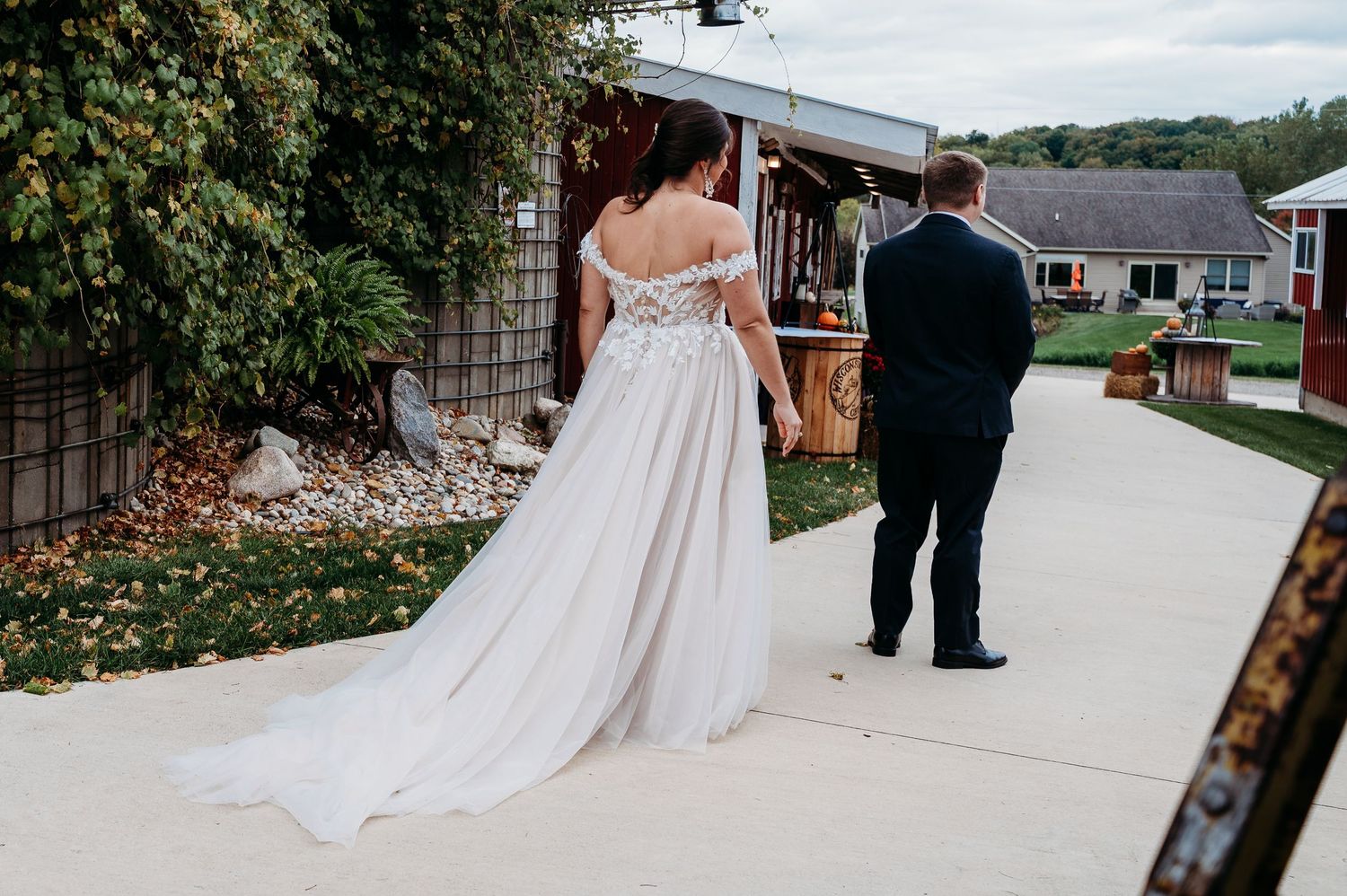 A bride in a flowing white gown and groom walk together on a path during their wedding day celebration.
