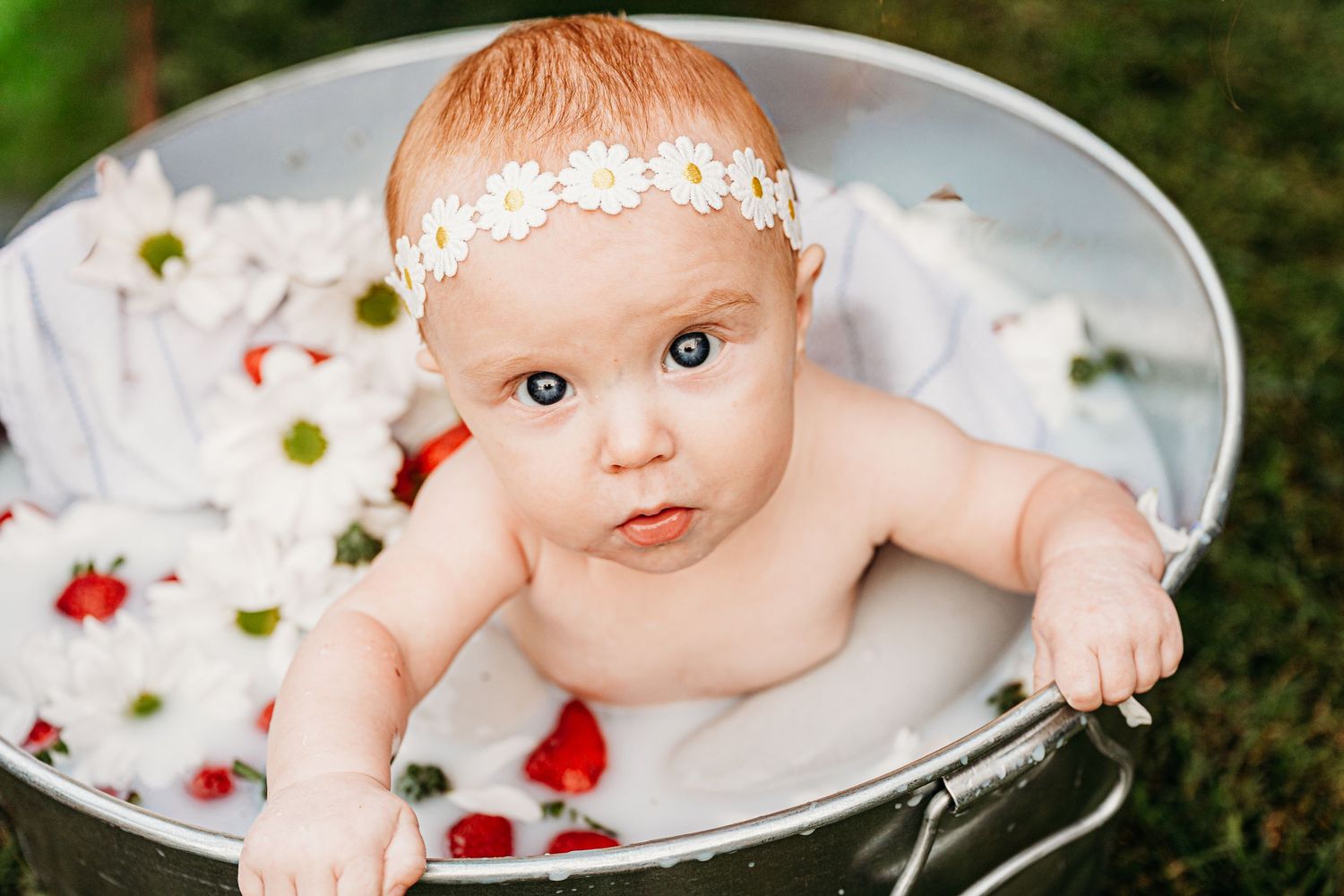 A baby in a milk bath photoshoot with floating flowers and a delicate floral headband.
