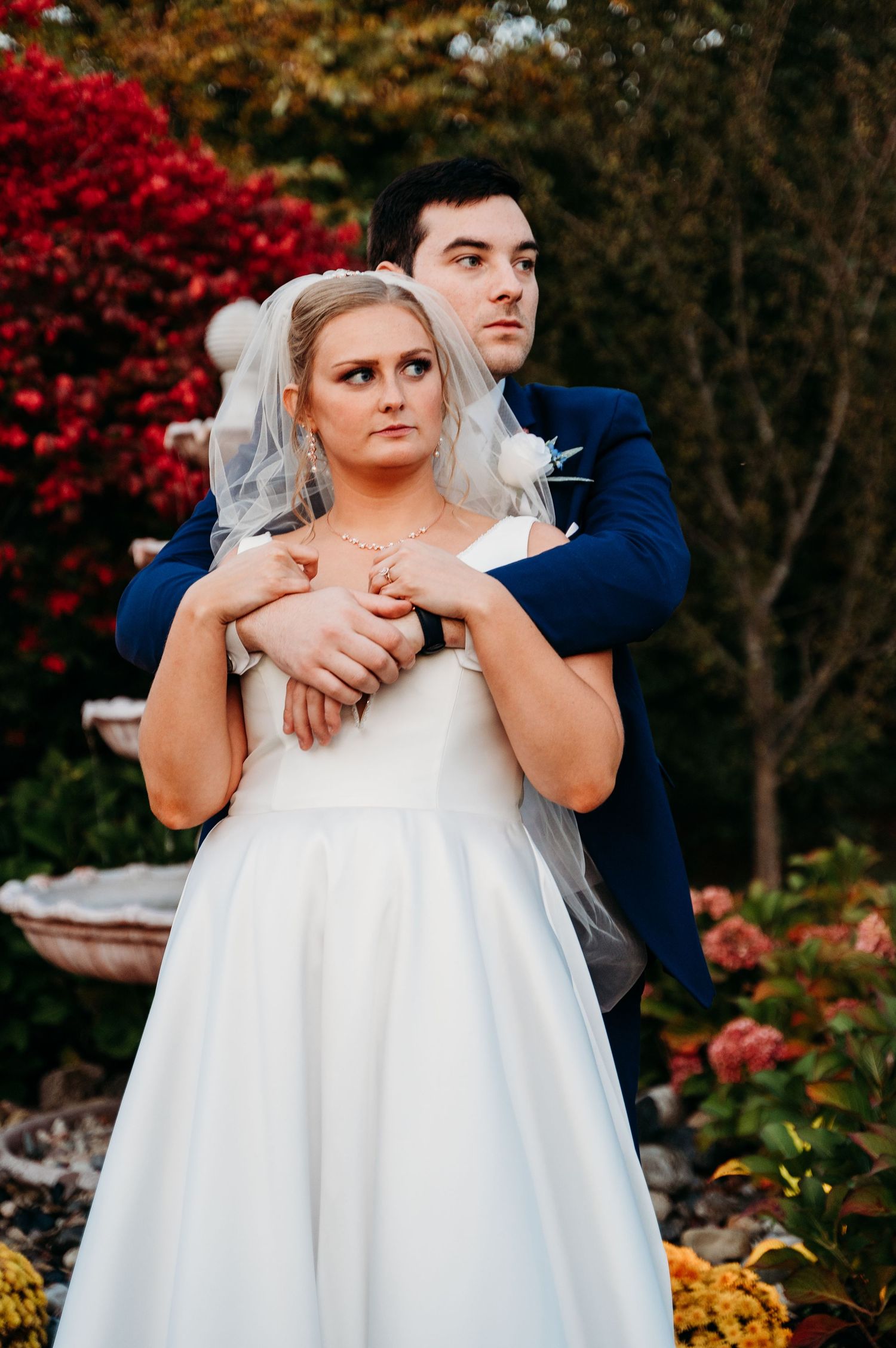 A romantic autumn wedding portrait with vibrant red foliage and garden florals in the background.