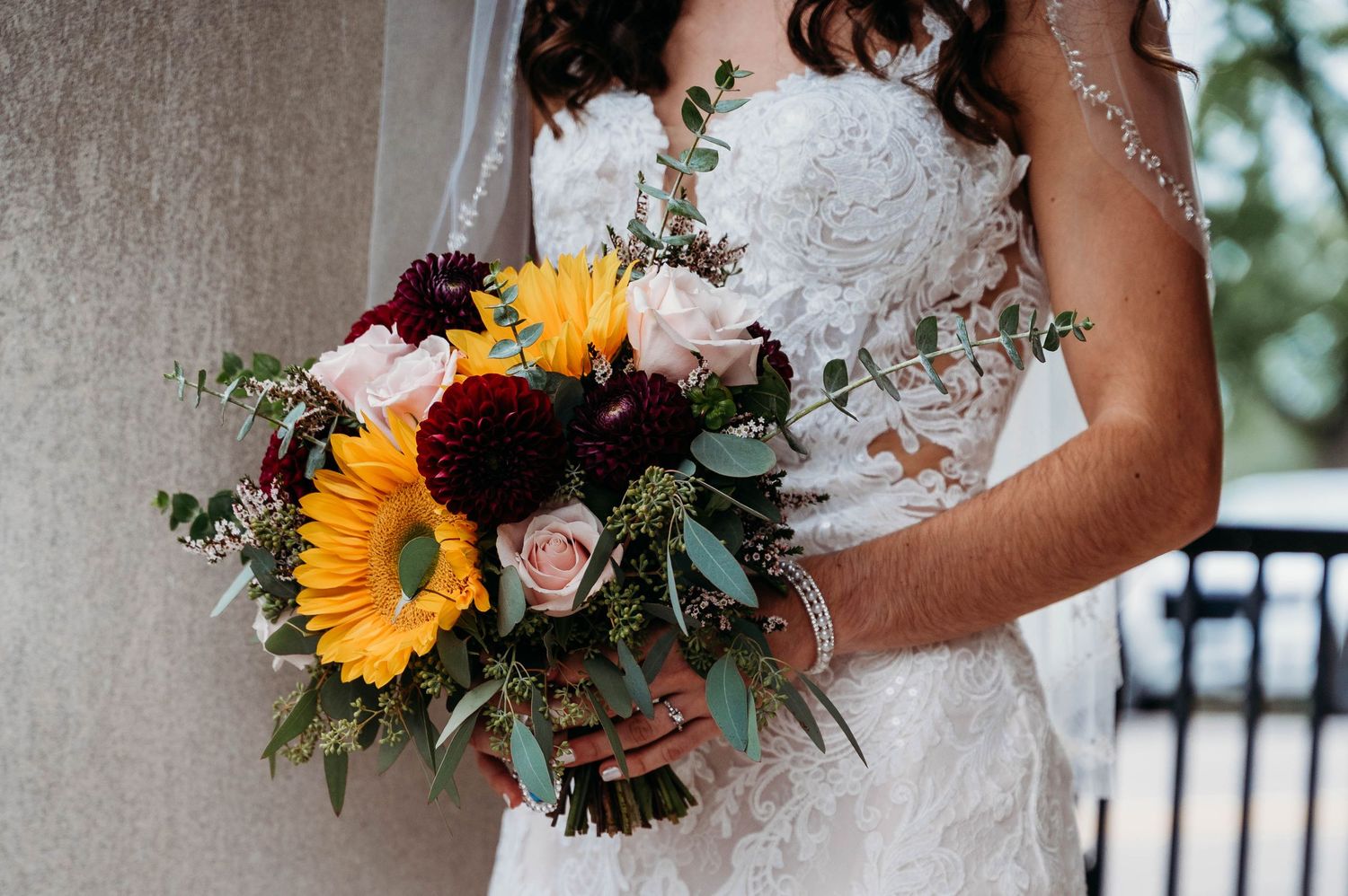 Bridal bouquet featuring vibrant sunflowers, blush roses and mixed greenery held against a white wedding dress.