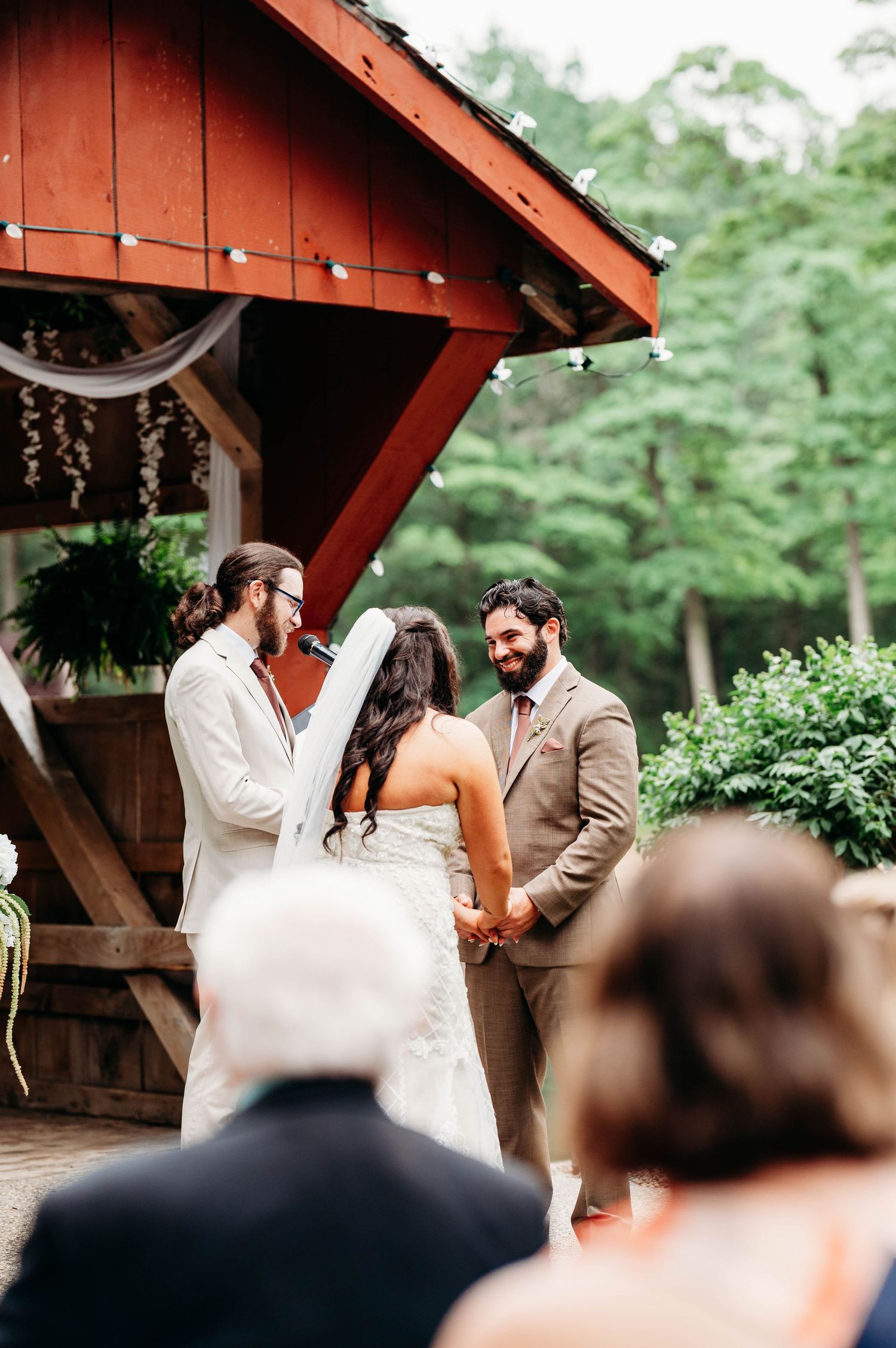 Couple exchanging vows at an outdoor rustic barn wedding ceremony surrounded by lush greenery.